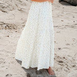 Woman in a white dress and straw hat standing on a sandy beach.