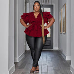 Woman in a red peplum top and black pants standing in a hallway.