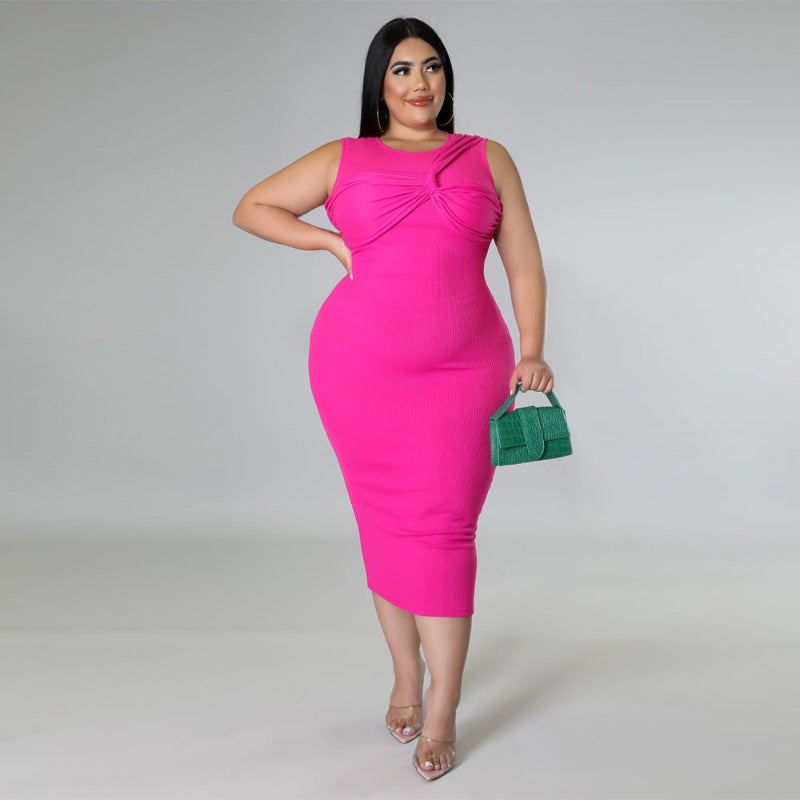 Woman wearing a bright pink dress holding a green clutch against a gray background