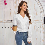 Woman in a white blouse with lace details holding a coffee cup, standing against a wooden door.
