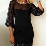 Black dress with sheer sleeves and sequin hem on a plain background