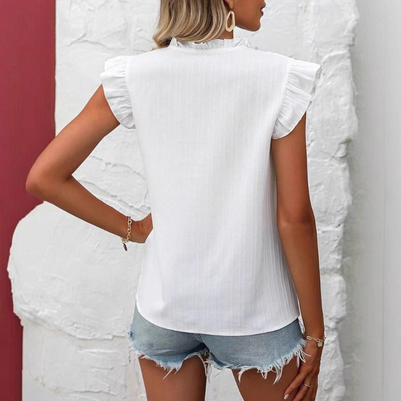 Close-up of a white sweetheart flutter sleeve embroidered blouse with delicate floral patterns.