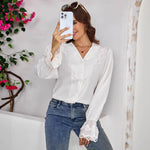 Woman taking a mirror selfie wearing a white blouse with lace details and blue jeans, with pink flowers in the background.