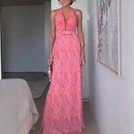 A woman from behind wearing a pink, backless, sleeveless midi dress with V-lace detailing on the back.