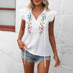Close-up of a white sweetheart flutter sleeve embroidered blouse with delicate floral patterns.
