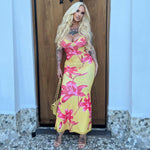 A yellow, printed strapless dress with a V-neck and a backless design. The dress is long and features a high-waist, shown laid flat to highlight the pattern and style.