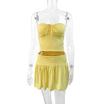 A light yellow off-shoulder tube top and a matching pleated short skirt set, displayed on a model or flat lay, showcasing a slim fit and elegant style.