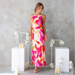 Woman modeling a one-shoulder printed sleeveless backless midi dress in lake blue, standing at sunset