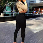 Person wearing a beige cropped top and black pants standing outdoors on a paved area.