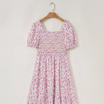 Pink floral dress on a hanger against a white background