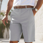 Person wearing light gray shorts, white shirt, and brown belt outdoors.