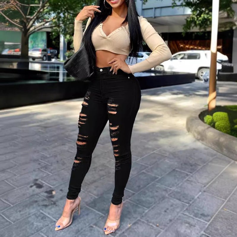 Woman wearing a beige crop top and black ripped jeans on a city street.