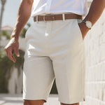 Person wearing a white shirt, beige shorts, and a brown belt with a blurred outdoor background.