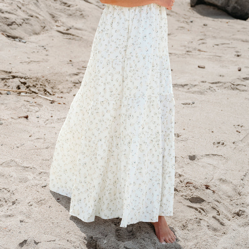 Woman in a white dress and straw hat standing on a sandy beach.