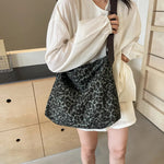 Close-up of a leopard print canvas tote bag with an adjustable strap, zipper closure, and visible interior pockets, displayed in a casual setting.