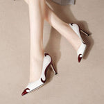 A close-up of a black satin high heel shoe with a pointed toe and a slender heel, featuring an embroidered white skull pattern and a dragonfly embellishment on the side.