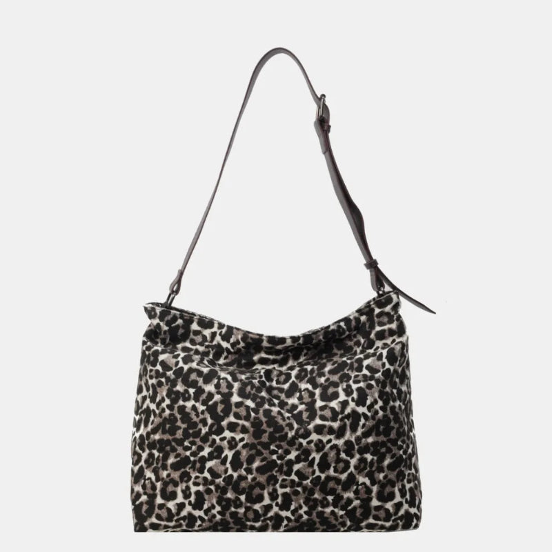 Close-up of a leopard print canvas tote bag with an adjustable strap, zipper closure, and visible interior pockets, displayed in a casual setting.