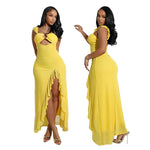 A full-length image of a woman wearing a flowing, long-sleeved, yellow maxi dress with a subtle side slit and a decorative hollow-out design on the bodice.
