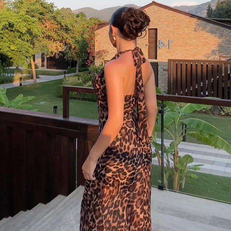 A sleeveless halter tie-back midi dress in a leopard print pattern, featuring a fitted silhouette and a belt at the waist. The dress is shown hanging, highlighting the full length and design details.