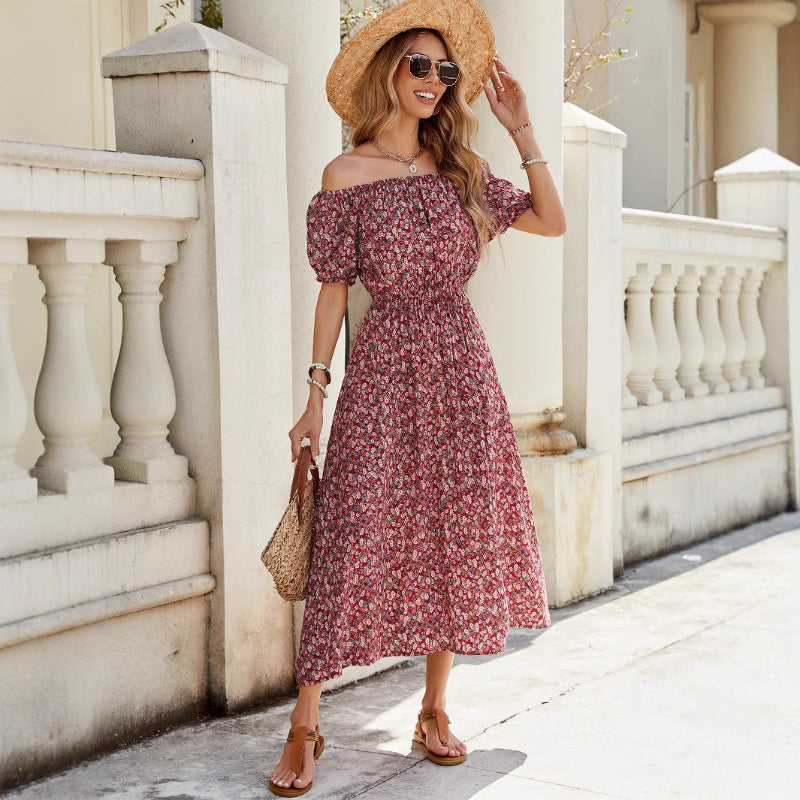 A full-length view of a person wearing a wine red, floral-printed, one-shoulder midi dress. The dress has a pleated A-line silhouette, an elastic waist, and a single short sleeve.