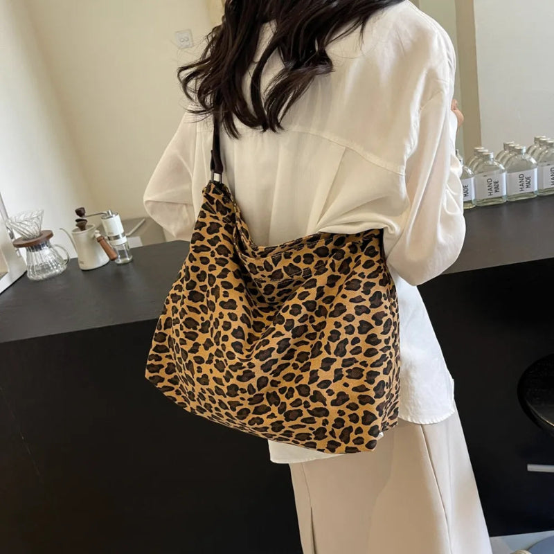 Close-up of a leopard print canvas tote bag with an adjustable strap, zipper closure, and visible interior pockets, displayed in a casual setting.