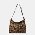Close-up of a leopard print canvas tote bag with an adjustable strap, zipper closure, and visible interior pockets, displayed in a casual setting.