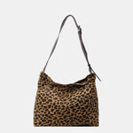 Close-up of a leopard print canvas tote bag with an adjustable strap, zipper closure, and visible interior pockets, displayed in a casual setting.