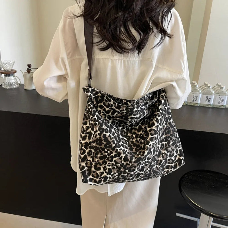 Close-up of a leopard print canvas tote bag with an adjustable strap, zipper closure, and visible interior pockets, displayed in a casual setting.