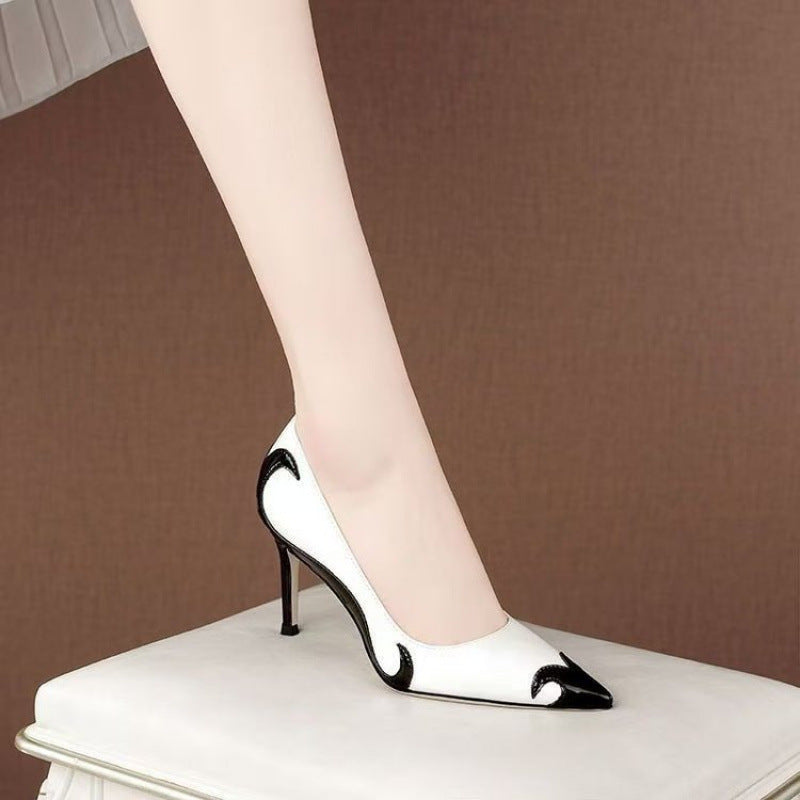 A close-up of a black satin high heel shoe with a pointed toe and a slender heel, featuring an embroidered white skull pattern and a dragonfly embellishment on the side.