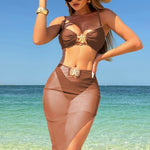 A model wearing a three-piece swimsuit set, which includes a bikini top, bikini bottoms, and a long mesh cover-up dress. The swimsuit is available in various colors and is shown in a beach setting.