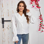 Woman wearing a white blouse with lace details and blue jeans, standing against a white wall with floral decorations.