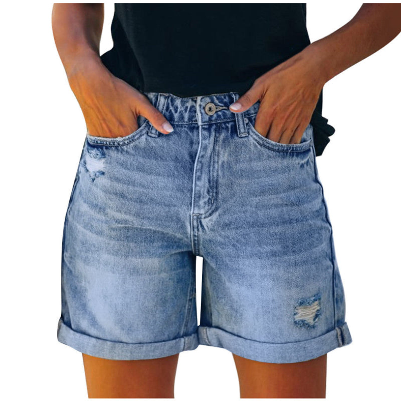 A pair of blue, high-waisted fringed denim shorts with distressed details. The shorts are laid flat on a neutral background, showcasing the style and texture. The fringe detailing is prominent along the hemline.