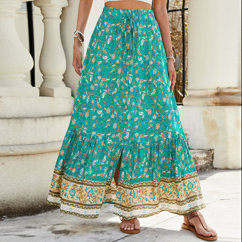 A high-waisted midi skirt with a bold digital print and a daring side slit, shown in a dark blue color. The skirt has snap buttons and is styled with a simple top.