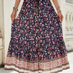 A high-waisted midi skirt with a bold digital print and a daring side slit, shown in a dark blue color. The skirt has snap buttons and is styled with a simple top.