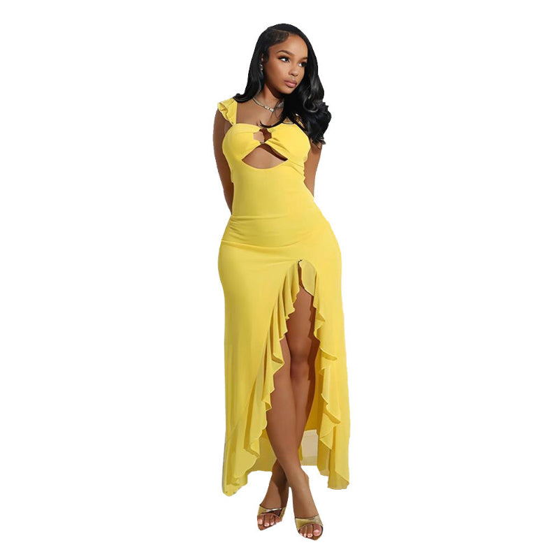 A full-length image of a woman wearing a flowing, long-sleeved, yellow maxi dress with a subtle side slit and a decorative hollow-out design on the bodice.