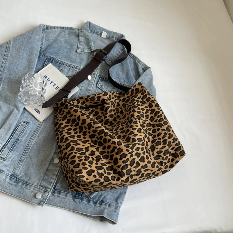 Close-up of a leopard print canvas tote bag with an adjustable strap, zipper closure, and visible interior pockets, displayed in a casual setting.