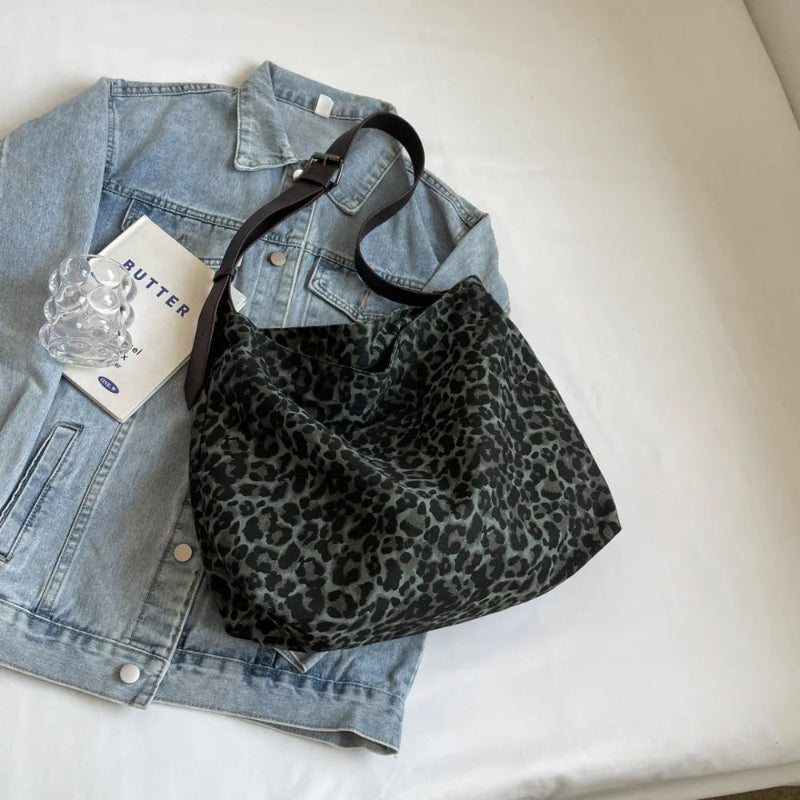 Close-up of a leopard print canvas tote bag with an adjustable strap, zipper closure, and visible interior pockets, displayed in a casual setting.