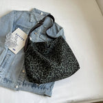 Close-up of a leopard print canvas tote bag with an adjustable strap, zipper closure, and visible interior pockets, displayed in a casual setting.