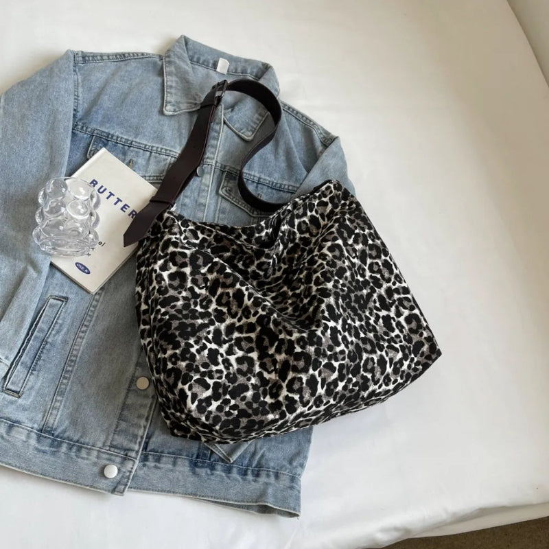 Close-up of a leopard print canvas tote bag with an adjustable strap, zipper closure, and visible interior pockets, displayed in a casual setting.