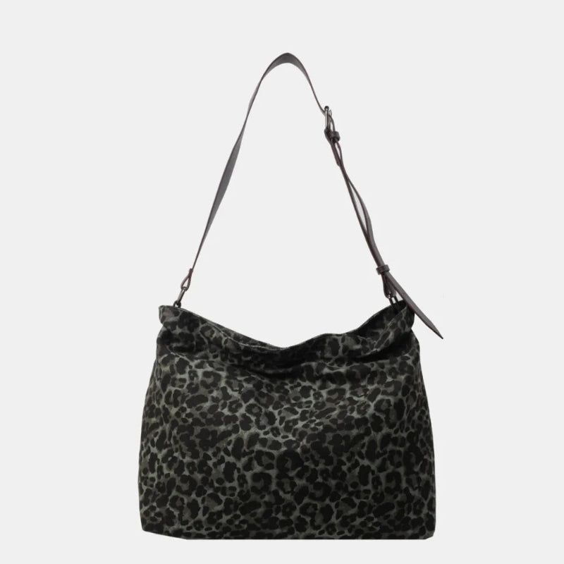 Close-up of a leopard print canvas tote bag with an adjustable strap, zipper closure, and visible interior pockets, displayed in a casual setting.