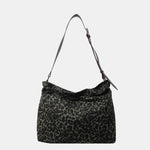 Close-up of a leopard print canvas tote bag with an adjustable strap, zipper closure, and visible interior pockets, displayed in a casual setting.