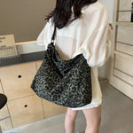 Close-up of a leopard print canvas tote bag with an adjustable strap, zipper closure, and visible interior pockets, displayed in a casual setting.