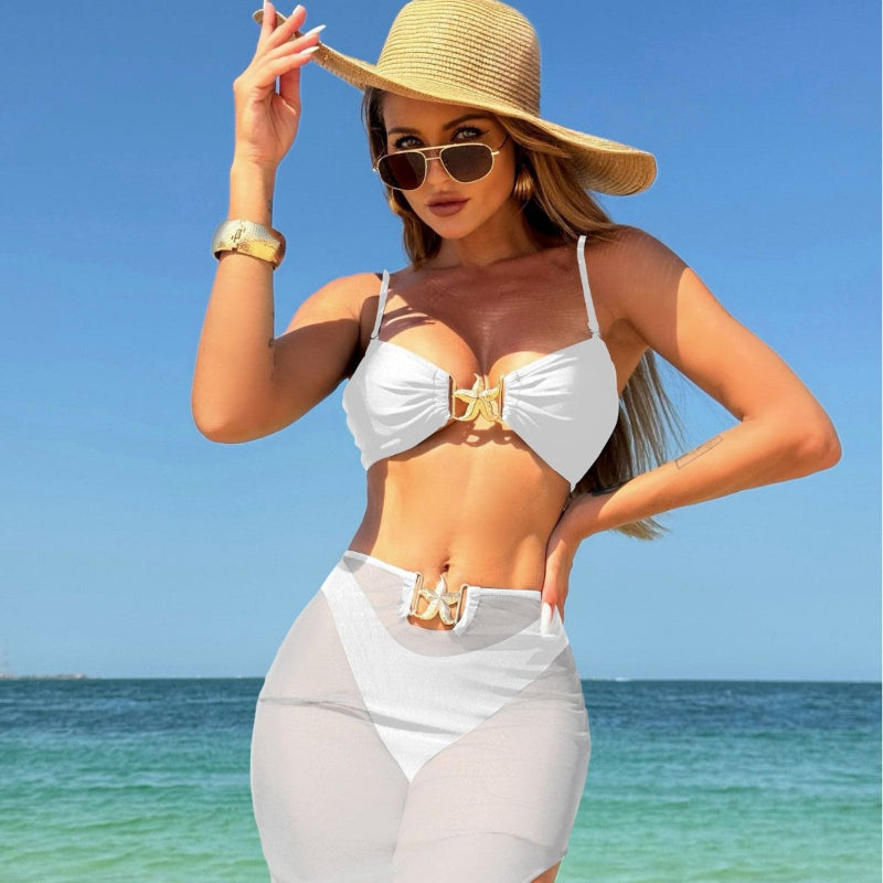 A model wearing a three-piece swimsuit set, which includes a bikini top, bikini bottoms, and a long mesh cover-up dress. The swimsuit is available in various colors and is shown in a beach setting.