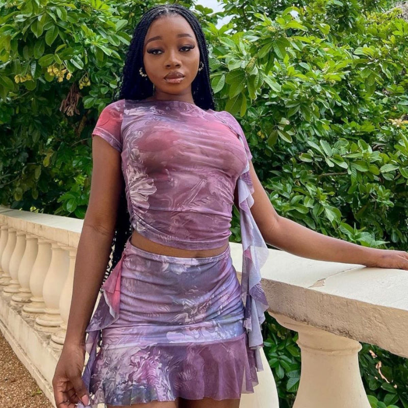 A woman wearing a purple fitted dress with a ruffle hem short top and matching mini skirt set, posing confidently.