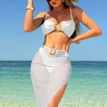 A model wearing a three-piece swimsuit set, which includes a bikini top, bikini bottoms, and a long mesh cover-up dress. The swimsuit is available in various colors and is shown in a beach setting.