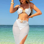 A model wearing a three-piece swimsuit set, which includes a bikini top, bikini bottoms, and a long mesh cover-up dress. The swimsuit is available in various colors and is shown in a beach setting.