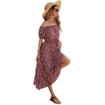 A full-length view of a person wearing a wine red, floral-printed, one-shoulder midi dress. The dress has a pleated A-line silhouette, an elastic waist, and a single short sleeve.