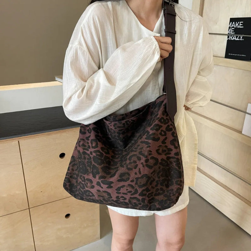 Close-up of a leopard print canvas tote bag with an adjustable strap, zipper closure, and visible interior pockets, displayed in a casual setting.