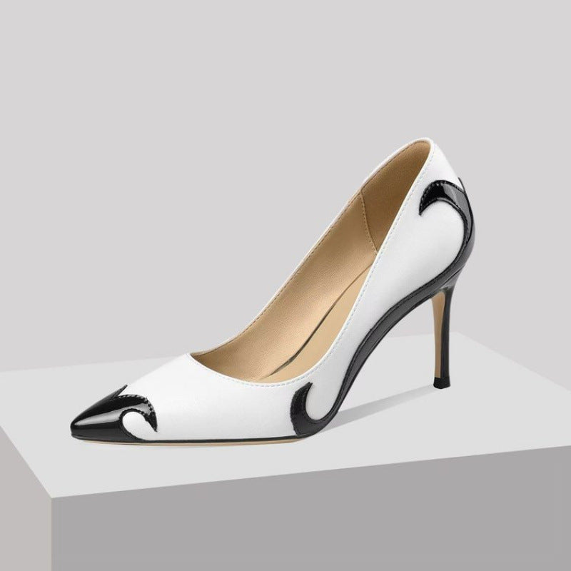 A close-up of a black satin high heel shoe with a pointed toe and a slender heel, featuring an embroidered white skull pattern and a dragonfly embellishment on the side.