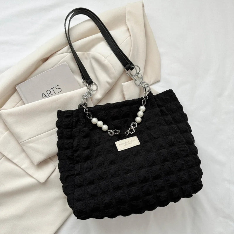 A close-up shot of a black bubble-textured tote bag with a chain detail, showcasing its unique surface and practical design.